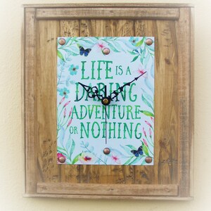 May include: A wooden framed clock with a white background and green floral design. The clock face reads "Life is a Daring Adventure or Nothing".