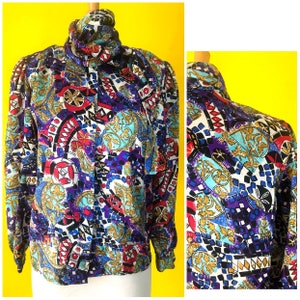 May include: A colorful, geometric patterned blouse with a high neck and long sleeves. The pattern features a mix of blue, red, gold, and white.