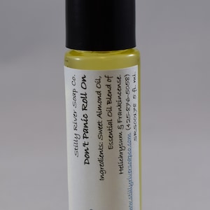 May include: A small, clear glass bottle with a black cap and a white label. The label reads "Don't Panic Roll On" and lists the ingredients as "Sweet Almond Oil, Essential Oil Blend of Helichrysum & Frankincense". The label also includes the company name "Stilly River Soap Co." and website address "www.stillyriversoapco.com".