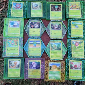 Op de afbeelding: Een set van 12 groene, blauwe en paarse hars Pokemon-kaarthouders. Elke houder heeft een ander Pokemon-personage en is versierd met glitter.