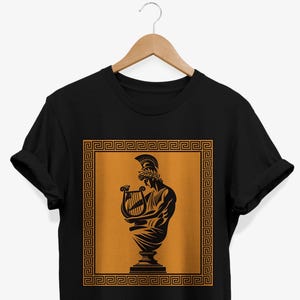 May include: Black t-shirt with a graphic of a Greek statue playing a lyre. The statue is inside a gold frame with a Greek key border.