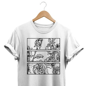 May include: White t-shirt featuring a black and white floral design. The design is divided into three horizontal rectangular panels, each showcasing detailed rose illustrations. The shirt is displayed on a wooden hanger.