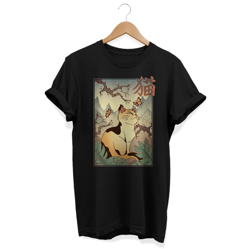 Puede incluir: Camiseta negra con un gr&aacute;fico de un gato sentado en un jard&iacute;n japon&eacute;s con mariposas y la palabra "猫" (gato en japon&eacute;s) encima.