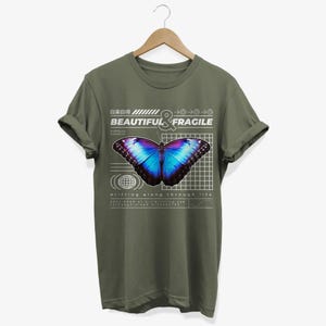 May include: A green t-shirt with a graphic of a blue and purple butterfly on a grid with the text "BEAUTIFUL & FRAGILE" and "drifting along through life".