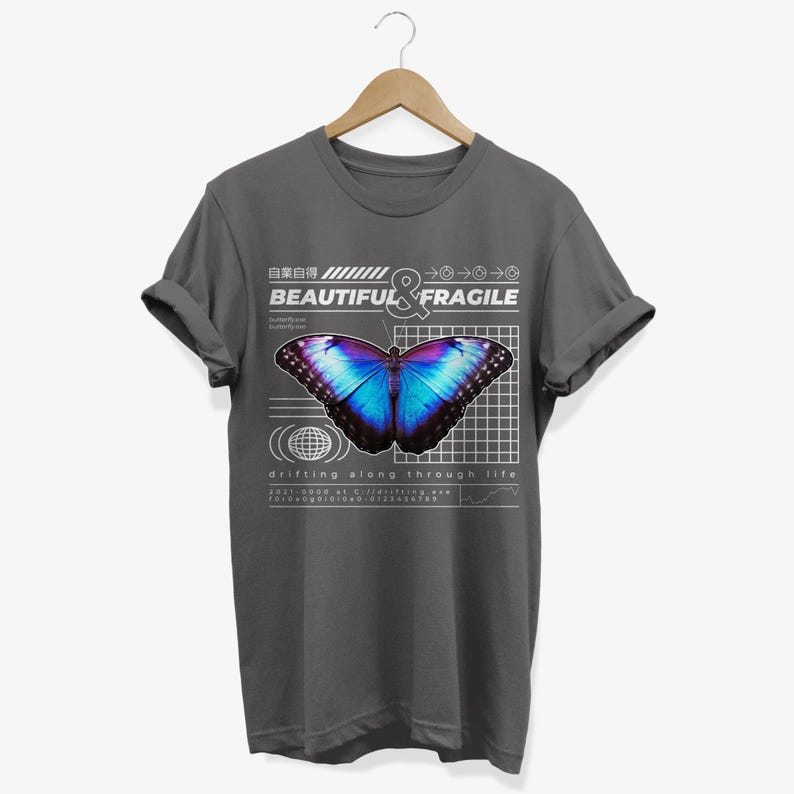 May include: A dark gray t-shirt with a graphic design featuring a blue and purple butterfly on a grid background. The text "BEAUTIFUL & FRAGILE" is printed above the butterfly, and the text "drifting along through life" is printed below the butterfly.