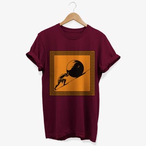May include: A maroon t-shirt with a graphic of a person pushing a large stone uphill. The graphic is framed by a gold Greek key border and set against a yellow background.