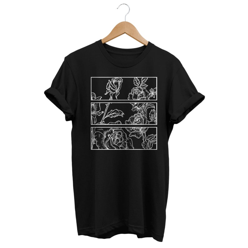 May include: Black t-shirt featuring a white floral design. The design is divided into three rectangular sections, each showcasing detailed line art of roses and foliage. The shirt is displayed on a wooden hanger against a white background.