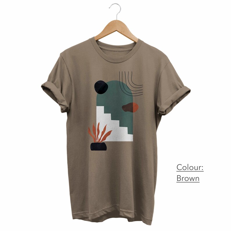 May include: A brown t-shirt with a graphic print of abstract shapes in shades of green, orange, white, and black. The text "Colour: Brown" is printed on the bottom right corner of the shirt.