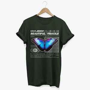 May include: A dark green t-shirt with a graphic design featuring a blue and purple butterfly with the text "BEAUTIFUL & FRAGILE" and "drifting along through life".