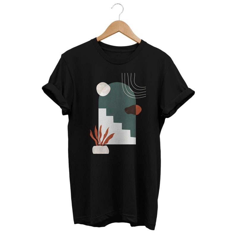 May include: Black t-shirt with a graphic design featuring abstract shapes in shades of green, brown, white, and orange. The design includes a stylized archway, steps, and a plant.