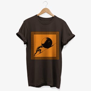 May include: A brown t-shirt with a graphic of a man pushing a large stone uphill. The graphic is surrounded by a gold Greek key border.