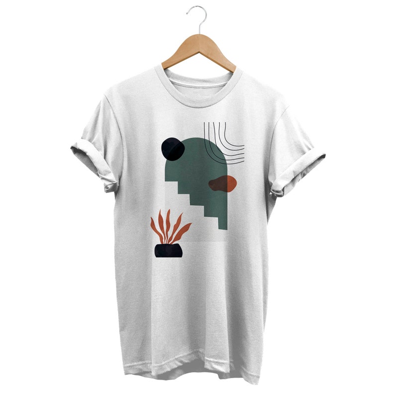 May include: White t-shirt with a graphic design featuring abstract shapes in green, black, orange, and brown. The design includes a curved line, a circle, and a plant.