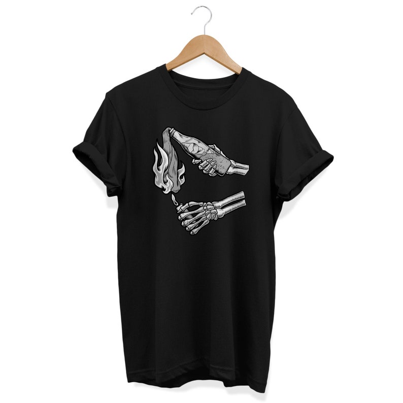 May include: Black t-shirt with a graphic of two skeletal hands, one holding a lit Molotov cocktail and the other reaching out to light it.