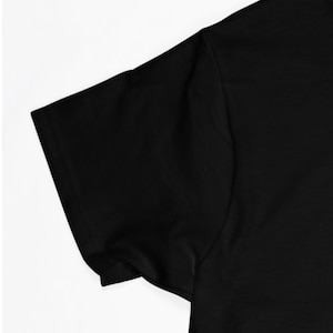 May include: Close-up of the black short sleeve of a t-shirt. The fabric is smooth and appears to be made of cotton.