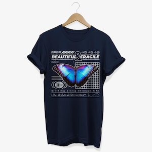 May include: Navy blue t-shirt with a graphic of a blue and purple butterfly on a grid pattern. The text "BEAUTIFUL & FRAGILE" is above the butterfly. The text "drifting along through life" is below the butterfly.