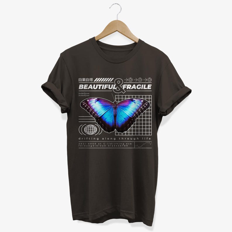 May include: A dark gray t-shirt with a graphic design featuring a blue and purple butterfly on a grid background. The text "BEAUTIFUL & FRAGILE" is above the butterfly, and the text "drifting along through life" is below the butterfly.