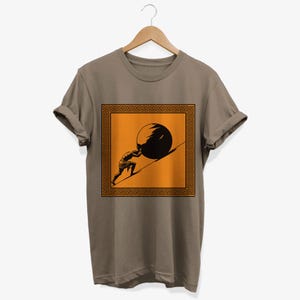 May include: A brown t-shirt with a graphic of a man pushing a boulder uphill. The graphic is framed with a Greek key border and set against an orange background.
