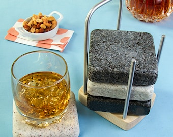 May include: A set of four gray and white stone coasters with a metal frame. The coasters are stacked on top of each other and are sitting on a wooden base.