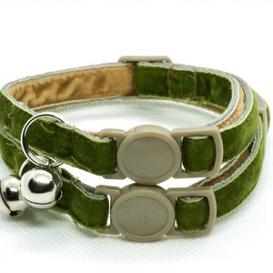 May include: A green velvet cat collar with a safety breakaway buckle and two silver bells. The collar is double-layered with a beige lining.