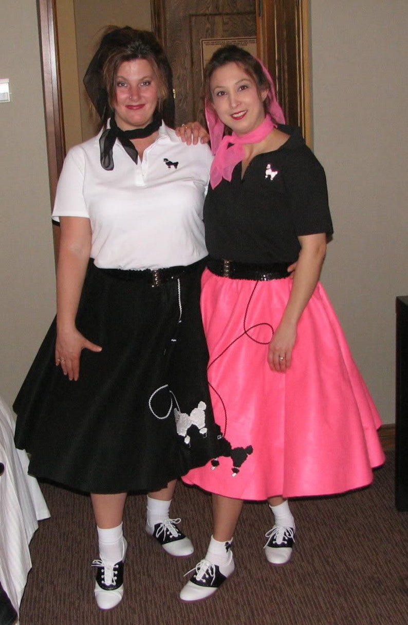 Pu&ograve; includere: Due donne che indossano gonne a ruota e camicie abbinate con disegni di barboncini. Una donna indossa una gonna nera e una camicia bianca con un papillon nero. L'altra donna indossa una gonna rosa e una camicia nera con un papillon rosa.