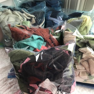 May include: Multiple plastic bags filled with various colors of fabric scraps. The bags are stacked on top of each other and are ready to be used for crafting projects.