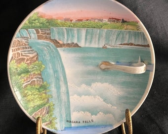 May include: A vintage ceramic plate with a painted image of Niagara Falls. The plate has a handle and the words "NIAGARA FALLS" are printed on the bottom.
