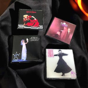 May include: Four square magnets featuring album art of Stevie Nicks. The magnets showcase album covers with images of Stevie Nicks in various poses and outfits. The color palette includes black, red, and white.