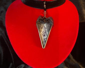 May include: A black velvet choker necklace with a silver chain and a triangular pendant. The pendant is made of glass and features a black and white image of a hand with a finger pointing upwards.
