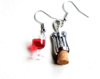May include: A pair of silver earrings with a wine glass and a corkscrew charm. The wine glass is filled with red liquid and the corkscrew has a cork attached to it.