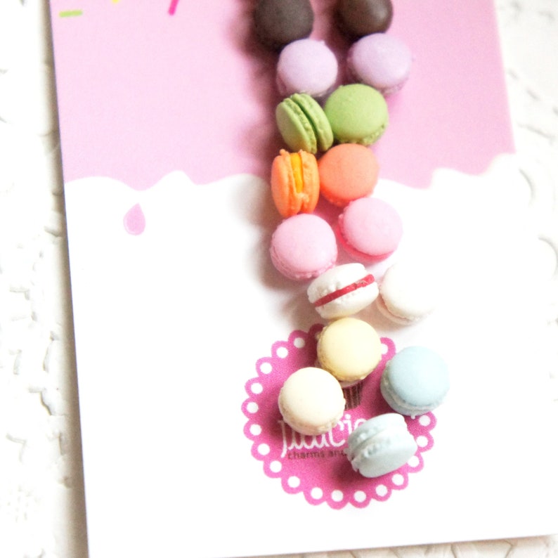 May include: A collection of colorful macarons, including pink, green, yellow, blue, and orange, arranged in a cascading pattern on a white background. The macarons are small and delicate, with a smooth, glossy finish.
