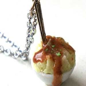 Peut inclure: Pendentif fantaisie représentant un petit bol de purée de pommes de terre et de sauce. Une petite cuillère en argent est insérée dans la nourriture. Le pendentif est suspendu à une chaîne en argent, créant un bijou original.