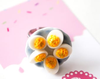 May include: A ring with a blue and white plate with six deviled eggs on it. The eggs are yellow with a white yolk.