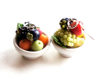 May include: Two miniature white bowls filled with colorful fruit, including grapes, berries, and oranges. The bowls are part of a set of earrings.