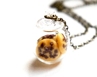 May include: A glass jar necklace with a bronze chain. The jar contains several chocolate chip cookies.