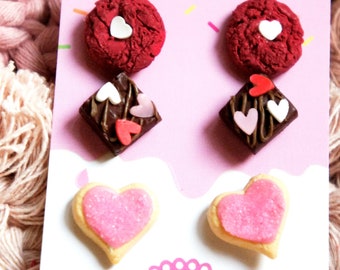 May include: A set of three pairs of earrings featuring miniature food designs. The earrings are made of polymer clay and feature a red velvet cupcake, a chocolate brownie, and a pink heart-shaped cookie.
