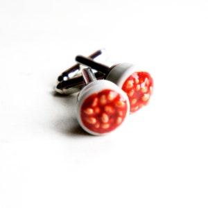 May include: A pair of silver cufflinks with a white ceramic top featuring a red design of baked beans in tomato sauce.
