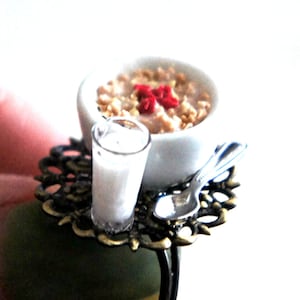 May include: A miniature breakfast ring with a bowl of cereal, a glass of milk, and a spoon on a decorative tray.