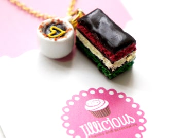 May include: A gold-colored chain necklace with two charms: a miniature white coffee cup with a yellow heart and a layered cake with red, white, green, and dark brown layers. A pink logo with the text "Jillicious charms and accessories" is visible.