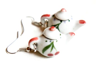 May include: A pair of white ceramic teapot earrings with red and green floral designs. The earrings are on a silver hook.