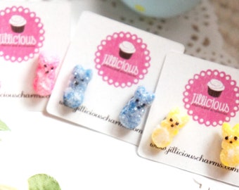 May include: A set of three pairs of earrings featuring pastel-colored gummy bear charms. The earrings are displayed on white cards with the text "jillicious" printed on them.