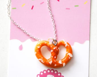 May include: A silver chain necklace with a pretzel-shaped pendant. The pretzel is orange and has white sprinkles on it.