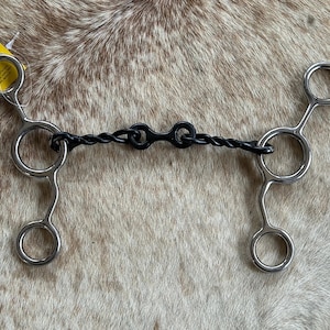 May include: A black twisted wire horse bit with two silver snaffle bits. The bit is designed for use with a horse's bridle.