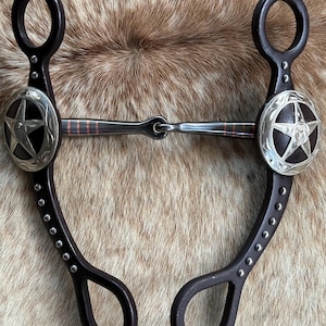 May include: A dark brown horse bit with a silver star design on each side. The bit has a stainless steel center and is decorated with small silver studs. The bit is designed for use with a horse.