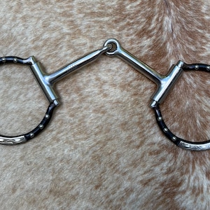 May include: A silver horse bit with black accents. The bit features a D-ring design with decorative silver patterns on the outer rings. The black accents are on the outer rings. The bit is designed for equestrian use.