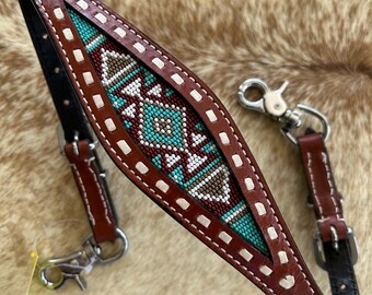 May include: A brown leather horse bridle with a turquoise, white, and brown beaded design. The bridle features white stitching and silver-colored metal hardware. The leather is a rich, warm brown color.