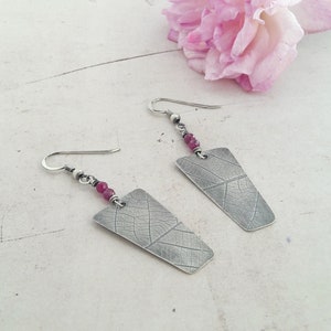 Peut inclure: Boucles d'oreilles en argent avec un motif de feuille et des perles roses. Les boucles d'oreilles sont de style pendantes et ont une fermeture à crochet.