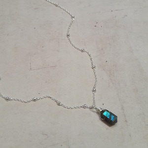 Op de afbeelding: Een zilveren ketting met een klein, iriserend labradorit-kristal hanger.