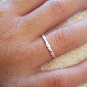 Könnte beinhalten: Ein dünner Silberring mit einer strukturierten, gehämmerten Oberfläche. Der Ring wird an einem Finger getragen.