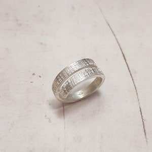 Könnte beinhalten: Ein silberner Ring mit einer strukturierten, gehämmerten Oberfläche. Der Ring besteht aus zwei ineinander verschlungenen Bändern.