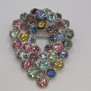 May include: A vintage brooch in a teardrop shape, adorned with a cluster of colorful, round rhinestones. The rhinestones are in shades of pink, blue, green, yellow, and purple, set in a silver-tone metal frame. A classic jewelry piece.